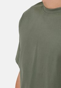 Olive green short-sleeved t-shirt made of cotton, featuring a smooth texture and a round neckline, with visible stitching details.