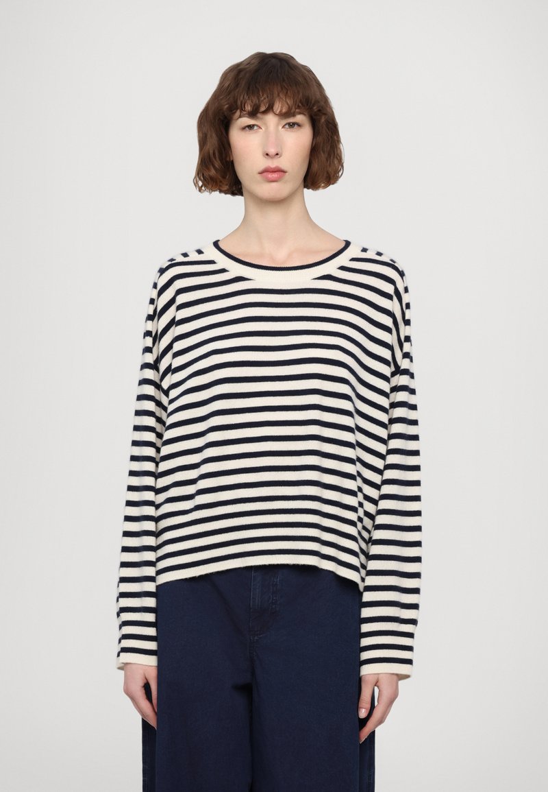 Maglione a righe manica lunga in crema e blu navy, con una vestibilità rilassata, scollatura rotonda e texture morbida. Indossato con pantaloni ampi blu scuro.