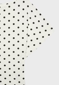 White fabric with evenly spaced small black polka dots, showing part of a short sleeve and neckline.