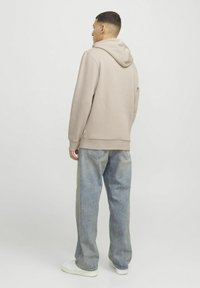 Beige hættetrøje med afslappet pasform, ribbede manchetter og en kængurulomme, parret med lyseblå løse jeans og hvide sneakers.