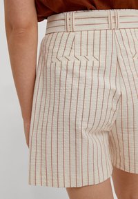 Shorts de couleur crème avec des rayures verticales marron, dotés d'une ceinture, d'une taille plate et d'une poche arrière unique avec un design embroché.