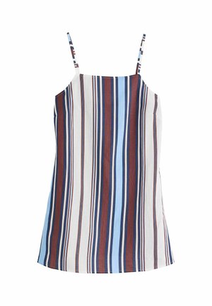 Femme portant un haut rayé sans manches et un pantalon large assorti, debout contre un mur blanc et un rebord en pierre sous un ciel bleu.
