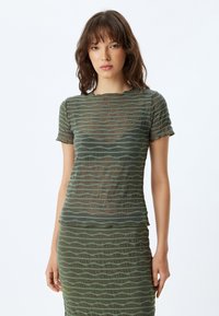 Top verde con patrón de olas, hecho de una tela texturizada, que presenta un escote redondo y mangas cortas. Transparente con diseño en capas.