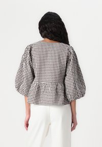 Blusa a quadri marroni e bianchi con maniche a palloncino e vita peplum. Realizzata in tessuto testurizzato, presenta un colletto quadrato.