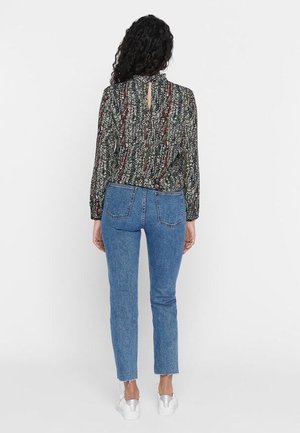 Patterned black and white blouse with long sleeves, keyhole back detail; paired with blue high-waisted jeans and white sneakers.