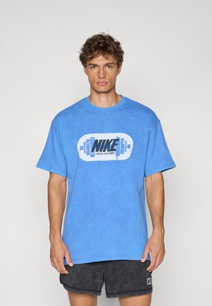Blue cotton t-shirt featuring a prominent black and white "Nike Athletic Department" logo. Short sleeves and relaxed fit, worn with gray shorts.