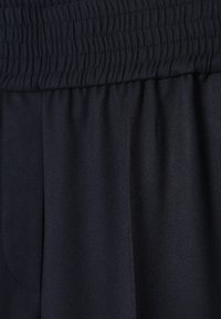 Gros plan de la ceinture élastique noire et de la couture de poche sur un pantalon en tissu foncé.