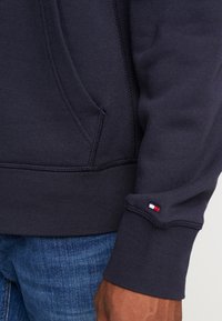 Sudadera marinera con bolsillo tipo canguro, puños de canalé y un pequeño acento de logo en rojo, blanco y azul en la manga. Tejido texturizado.