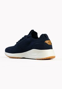 Sneakers lavorati a maglia blu navy con tomaia texture e suola grigio chiaro. Presentano un accento in pelle marrone sul tallone. Design leggero.