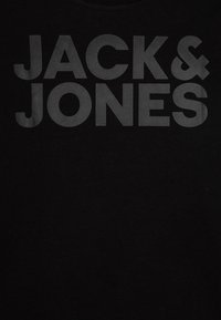 Juodas marškinėlis su dideliu, ryškiu, tamsiai pilku tekstu „JACK & JONES“, užrašytu be serifų šriftu. Sklandaus audinio tekstūra, apvalios apykaklės dizainas.