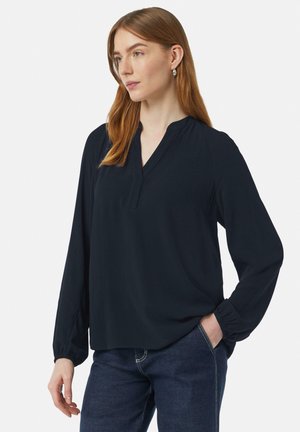Marineblauw blouse met lange mouwen, een V-hals en een ontspannen pasvorm. Gemaakt van zachte stof met elastische boorden en vlakke naden. Gecombineerd met donkere jeans.