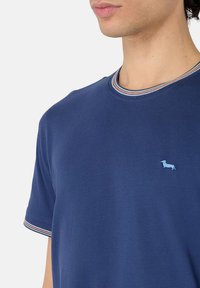 T-shirt blu navy in morbido tessuto con maniche corte, caratterizzato da un ricamo di un cane azzurro e un colletto a costine con strisce rosse e bianche.