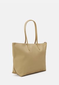 Sac fourre-tout beige en matériau synthétique lisse, avec deux longues poignées et une fermeture éclair. Forme rectangulaire avec une texture subtile.