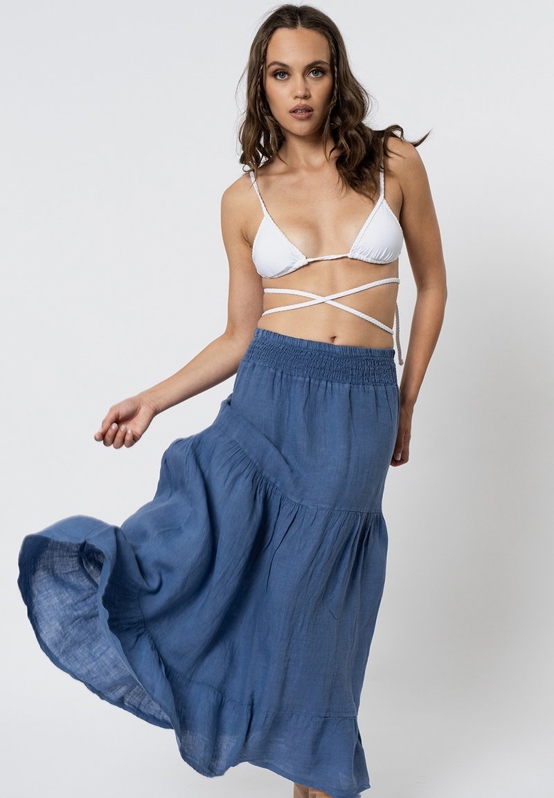 Gonna maxi blu realizzata in tessuto leggero, caratterizzata da un design a strati con un orlo fluente. Il modello indossa un bikini bianco con spalline.