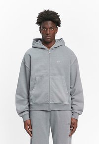 Gray zip-up hoodie made from soft cotton. Features a hood, kangaroo pockets, and ribbed cuffs, with a small logo on the chest.