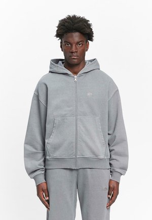 Gray zip-up hoodie made from soft cotton. Features a hood, kangaroo pockets, and ribbed cuffs, with a small logo on the chest.