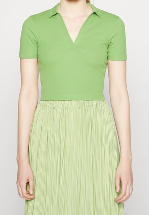 Grünes kurzärmeliges Poloshirt mit V-Ausschnitt und Kragen, kombiniert mit einem plissierten hellgrünen Rock. Glatter Stoff aus Baumwollmischung.