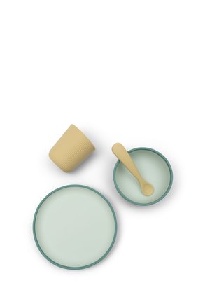 Tasse beige, cuillère beige dans un petit bol avec un bord vert, et une grande assiette avec un bord vert sur fond blanc.