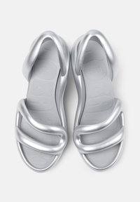 Silver sandals with a cushioned sole, featuring three curved straps, smooth texture, and a rounded design. Brand logo visible on insole.
