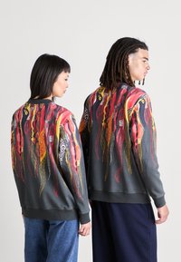 Gray sweatshirt featuring a vibrant abstract design in red, yellow, and black with dotted accents. Ribbed cuffs and hem. Unisex style.