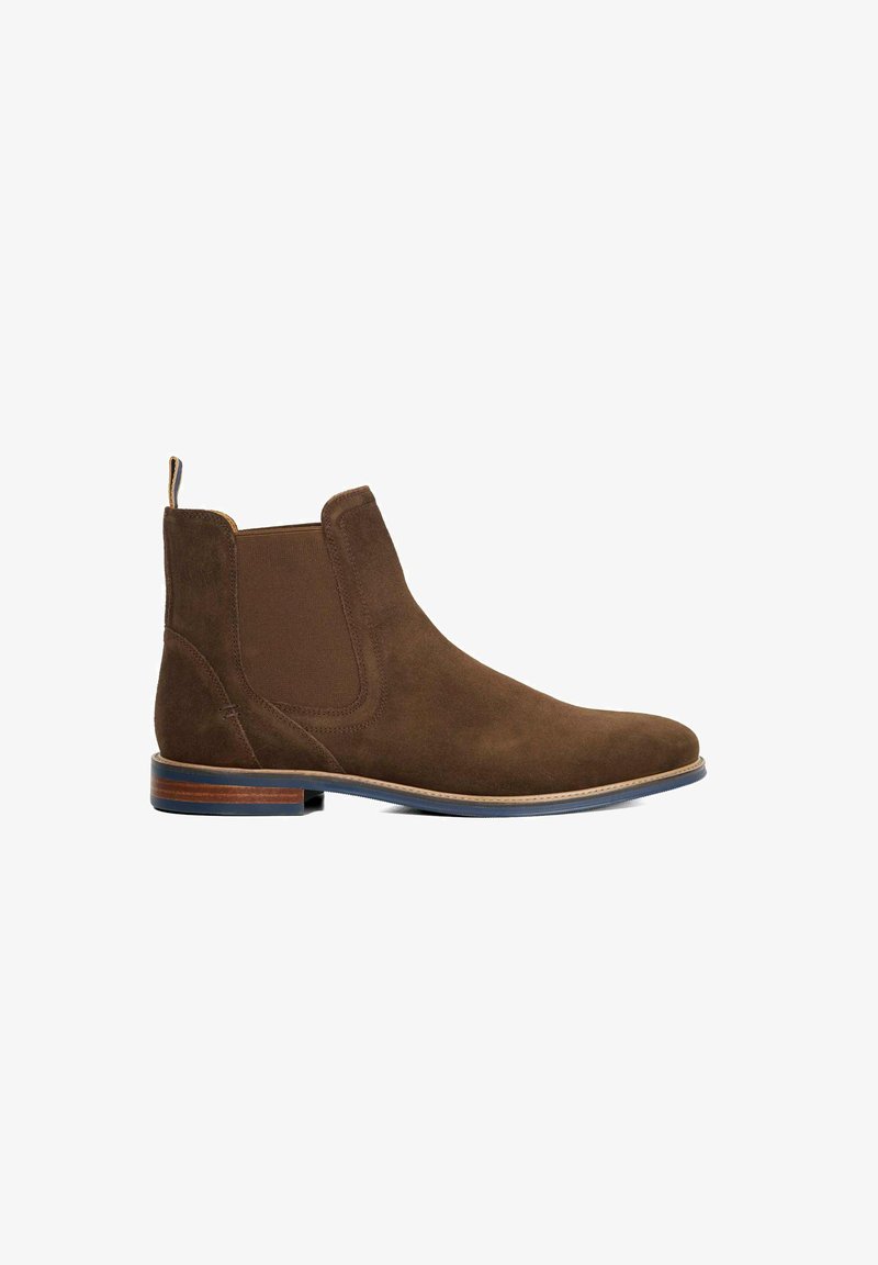 Bottine en suède marron avec des panneaux élastiques sur les côtés, bout rond, talon en bois contrasté et texture lisse. Dotée d'une languette à l'arrière.