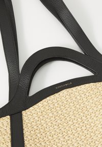 Gef lochtene Strohtasche mit schwarzen Lederelementen und doppelten Trägern. Verfügt über einen abgerundeten Griff mit Aussparung und ein prägedrucktes Logo auf dem Leder.