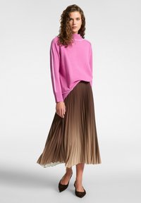 Maglione rosa lavorato a maglia con colletto alto, abbinato a una gonna plissettata in ombre tan che passa da scuro a chiaro, e scarpe ballerine marroni a punta.