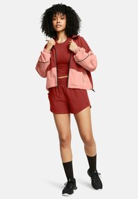 Sportliche Kleidung bestehend aus einer pinken Jacke, einem roten Oberteil und passenden roten Shorts. Das Material wirkt leicht und verfügt über elastische Akzente sowie ein sportliches Design.