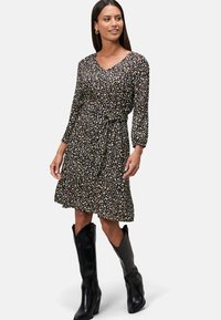 Robe noire à fleurs avec des manches bouffantes trois-quarts, taille cintrée et jupe évasée ; associée à des bottes noires montantes.