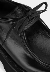 Zwarte leren schoen met een gladde, glanzende afwerking, ronde neus en platte veters die door oogjes zijn geregen, met stiksels langs de zool.