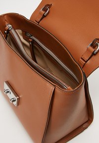 Sac à main en cuir texturé brun avec des accessoires en métal argenté, comportant deux compartiments zippés et une section centrale ouverte.