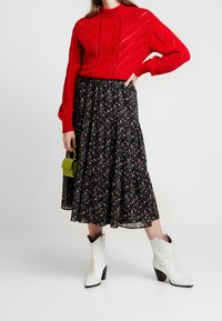 Röd stickad tröja med hög halsringning; svart blommig kjol med utsvängd nederkant; vita klackstövlar; liten grön handväska.