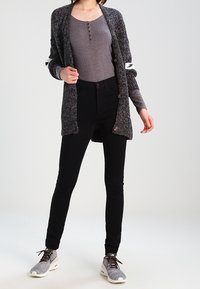 Gray knitted cardigan with buttons, over a gray ribbed top, paired with black skinny jeans and gray sneakers. Cardigan has white accents.