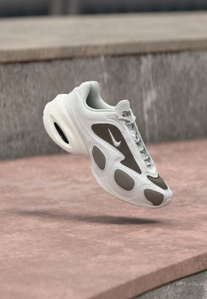 Baskets Nike blanches et grises flottant au-dessus d'une surface en pierre, avec un devant à lacets et un coussin d'air visible dans la semelle.