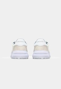 Lacoste sneakers featuring a light beige suede upper, white accents, a cushioned sole, and lace-up design, seen from the rear.
