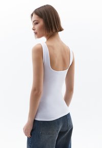 Witte, aansluitende tanktop met brede banden en een ronde rug, gecombineerd met hoog uitgesneden, losse denim jeans. Gladde stof en strakke lijnen.