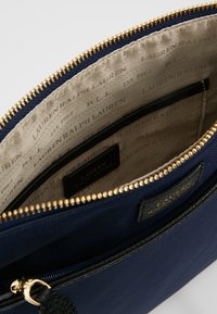 Interno di una borsa in tessuto blu navy con zip dorata, fodera beige con logo del marchio e un'etichetta in pelle nera con testo impresso.