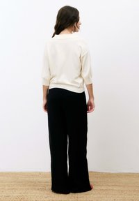 Pull en tricot de couleur crème avec un col polo, associé à un pantalon large noir. Texture douce, détails côtelés sur la ceinture du pantalon.