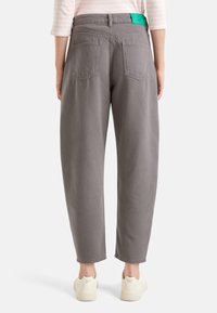 Šedé denimové kalhoty s volným střihem, které mají na pásku zelenou nášivku a čtyři zadní kapsy. Nosí se s bílými teniskami.