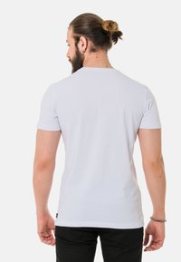 Weißes T-Shirt mit kurzen Ärmeln in normaler Passform, aus Baumwolle, mit Rundhalsausschnitt und einem kleinen Logo-Tag auf der linken Seite in der Nähe des Saums.