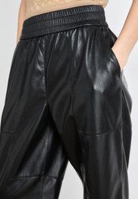 Μαύρο δερμάτινο παντελόνι με λεία υφή, διαθέτει ελαστική μέση και πλαϊνές τσέπες. Τα υλικά προσφέρουν κομψή εμφάνιση.