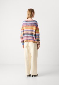 Mehrfarbiger Strickpullover mit horizontalen Streifen, lockere Passform, weiter Ausschnitt und gerippten Bündchen, kombiniert mit hochtaillierten beigen Hosen.