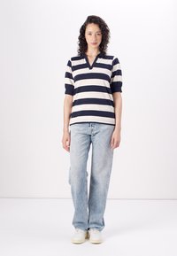 Gestreepte top met korte mouwen in marineblauw en crème, met een V-hals. Draagt met lichtblauwe rechtvaardige jeans en witte sneakers.