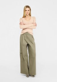 Hele-roosa nööpidega kardigan, mis on kombineeritud laia lõikega õlivihmroheliste cargo-pükstega, millel on küljetasku ja avar lõige. Komplekti lõpetavad madalad mustrilised kingad.