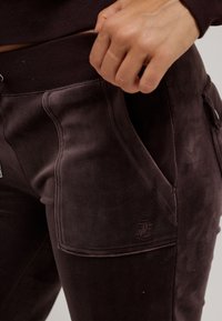 Donkerbruine sweatpants van zacht stof, met een hoge tailleband, zijzakken en een geborduurd logo op de voorzak.