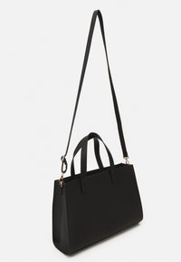 Bolsa tote negra con asas cortas y una correa larga ajustable. Hecha de material suave con costuras mínimas y detalles de hardware en tono dorado.