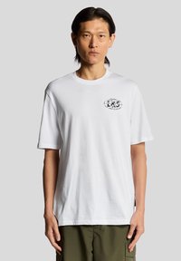 Witte katoenen t-shirt met korte mouwen, ronde hals, met een zwart logo op de linkerkant van de borst. Gepaard met olijfgroene cargobroek.