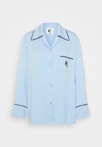 Ανοιχτό μπλε πιτζάμα με κουμπιά στο μπροστινό μέρος, παρεκκλίνων γιακά, μακριά μανίκια, σκούρα μπλε ρέλι και τσέπη στο στήθος με μικρό λογότυπο.