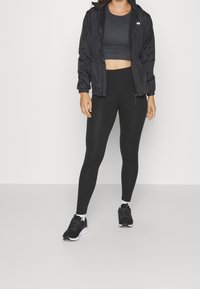 Sort letvægtsjakke med elastiske manchetter og talje, parret med en mørkegrå crop top og sorte leggings. Sorte sportssko vises.