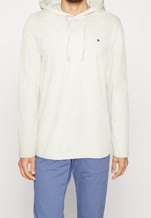Felpa bianca in cotone con tasca frontale, cappuccio con cordino e piccolo logo ricamato sul petto. Abbinata a pantaloni azzurri chiari.